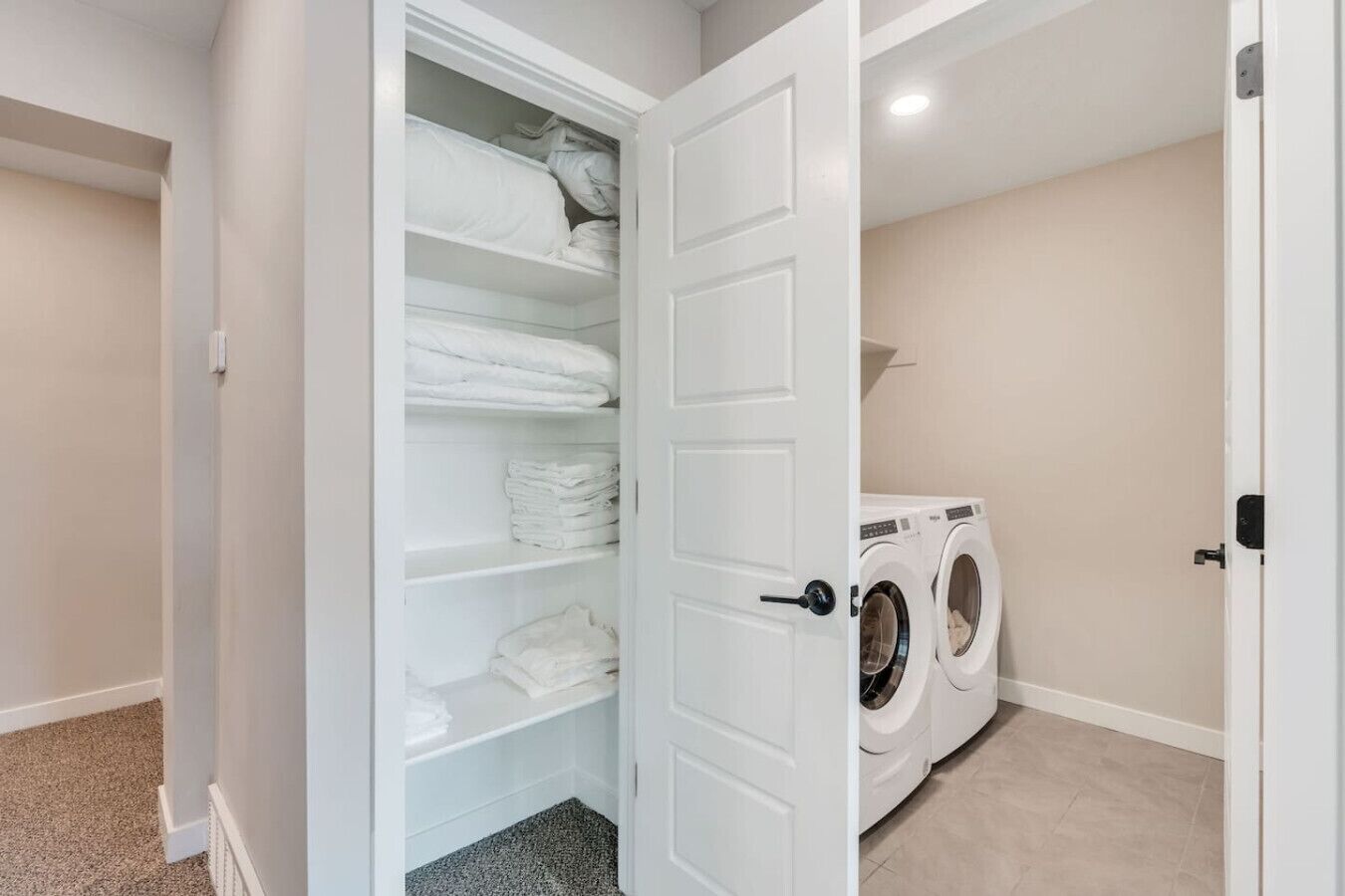 Un cuarto de lavandería con una lavadora y un armario blanco con estantes.