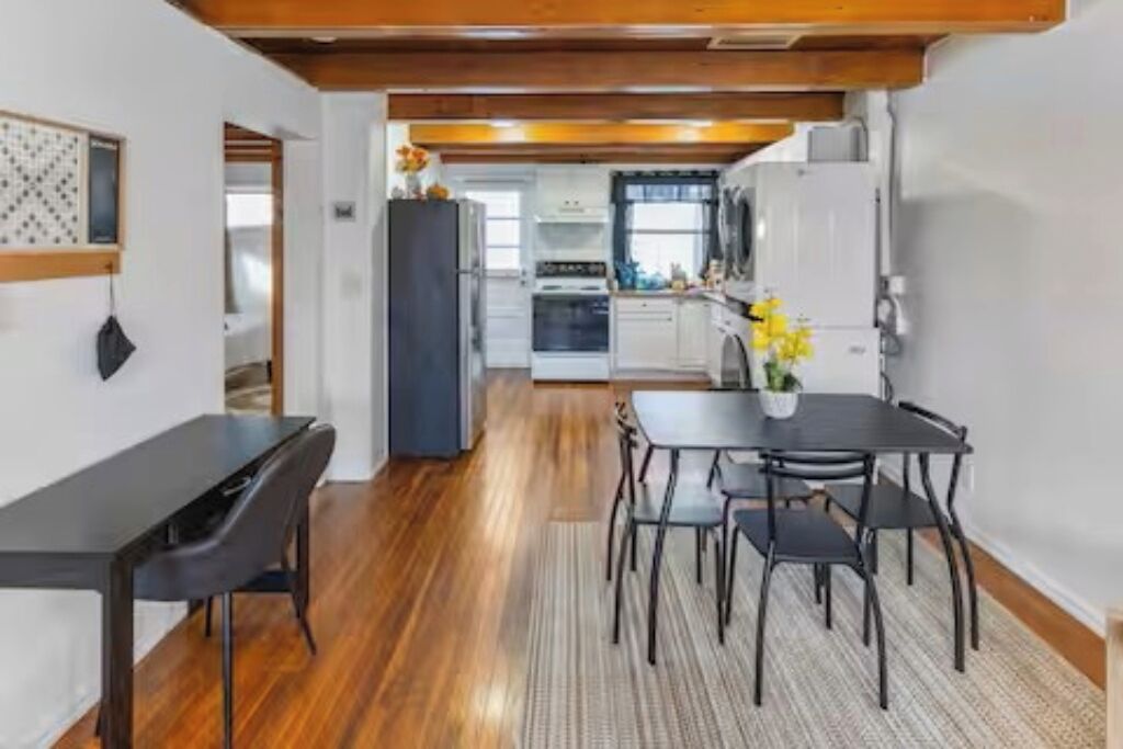 A modern kitchen with white cabinets, a black refrigerator, and a dining area with a black table and chairs.