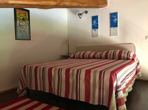 Ein Bett mit gestreifter Bettdecke, ein Nachttisch mit Lampe und Wandbild.
