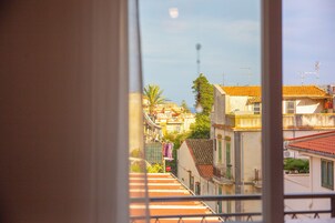 Vista a través de una ventana mostrando una zona residencial con edificios, una palmera y una señal de calle.