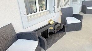 En balkong med möbler i rotting, ett bord med en lampa och ett fönster med fönsterluckor.