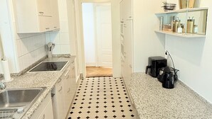 Ett smalt kök med vita skåp, en bänkskiva i granit och ett svart- och vitrutigt golv.