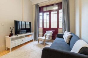 Ein Wohnzimmer mit Fernseher, weißem Unterhaltungsschrank, grauem Sofa und einer roten Tür.