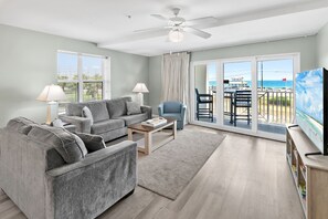 Ein Wohnzimmer mit grauem Sofa, einem Couchtisch, einem Fernseher und einem Balkon mit Meerblick.