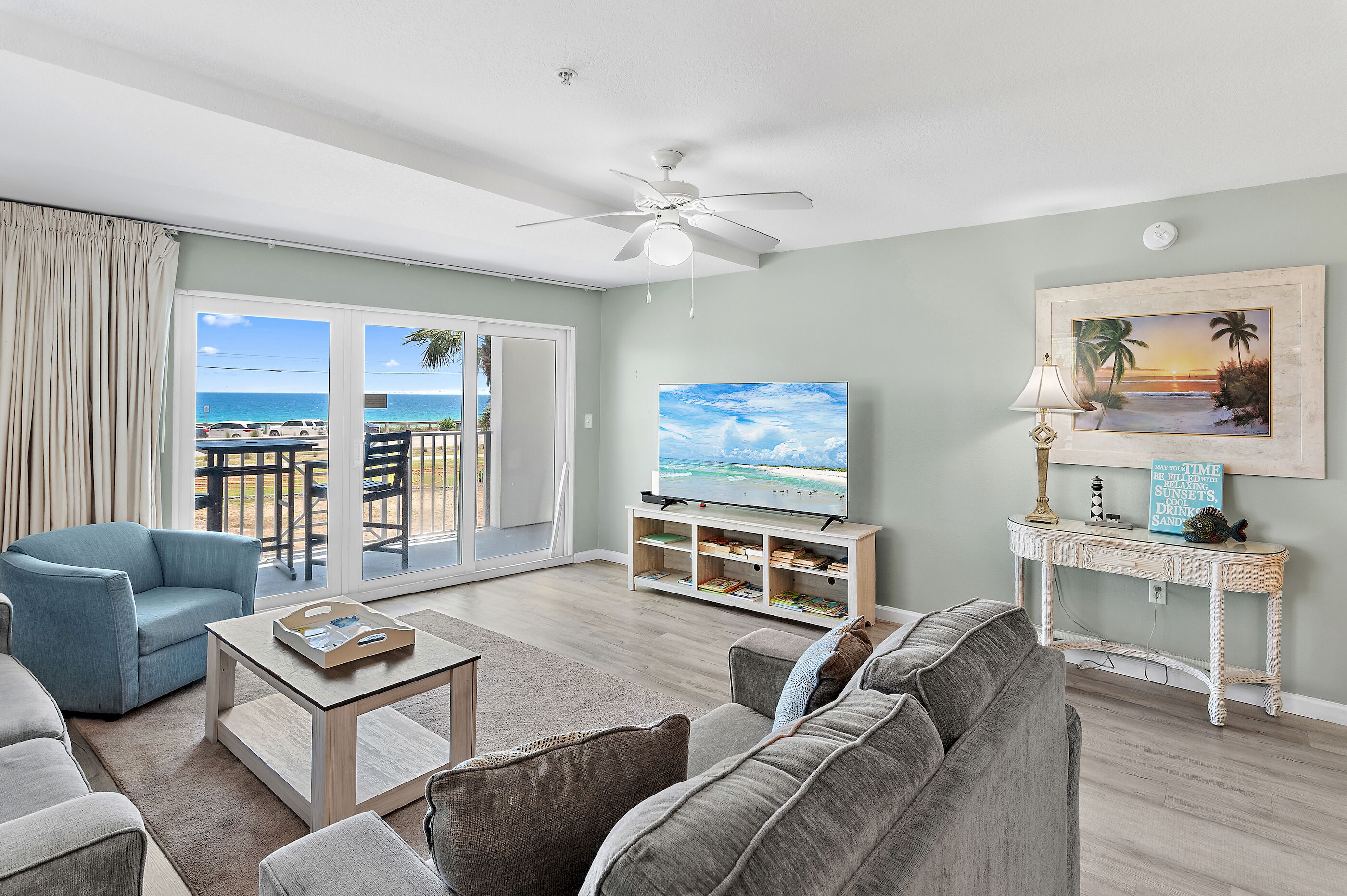 A living room with a TV, sofa, coffee table, and a view of the ocean through large windows.