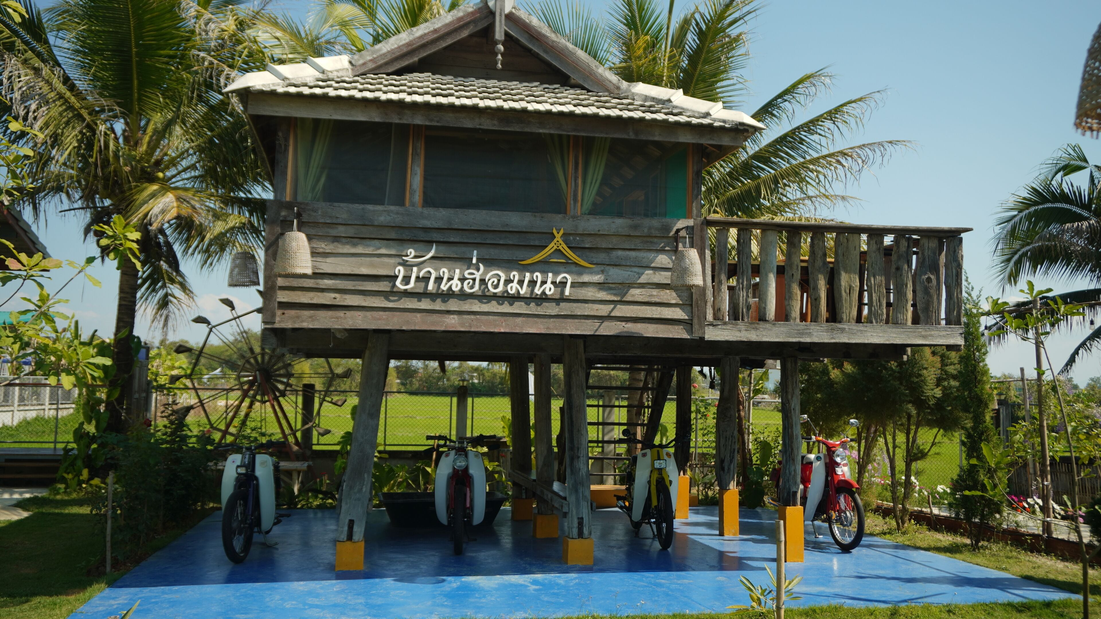 A wooden structure with a balcony, surrounded by palm trees and a blue floor.