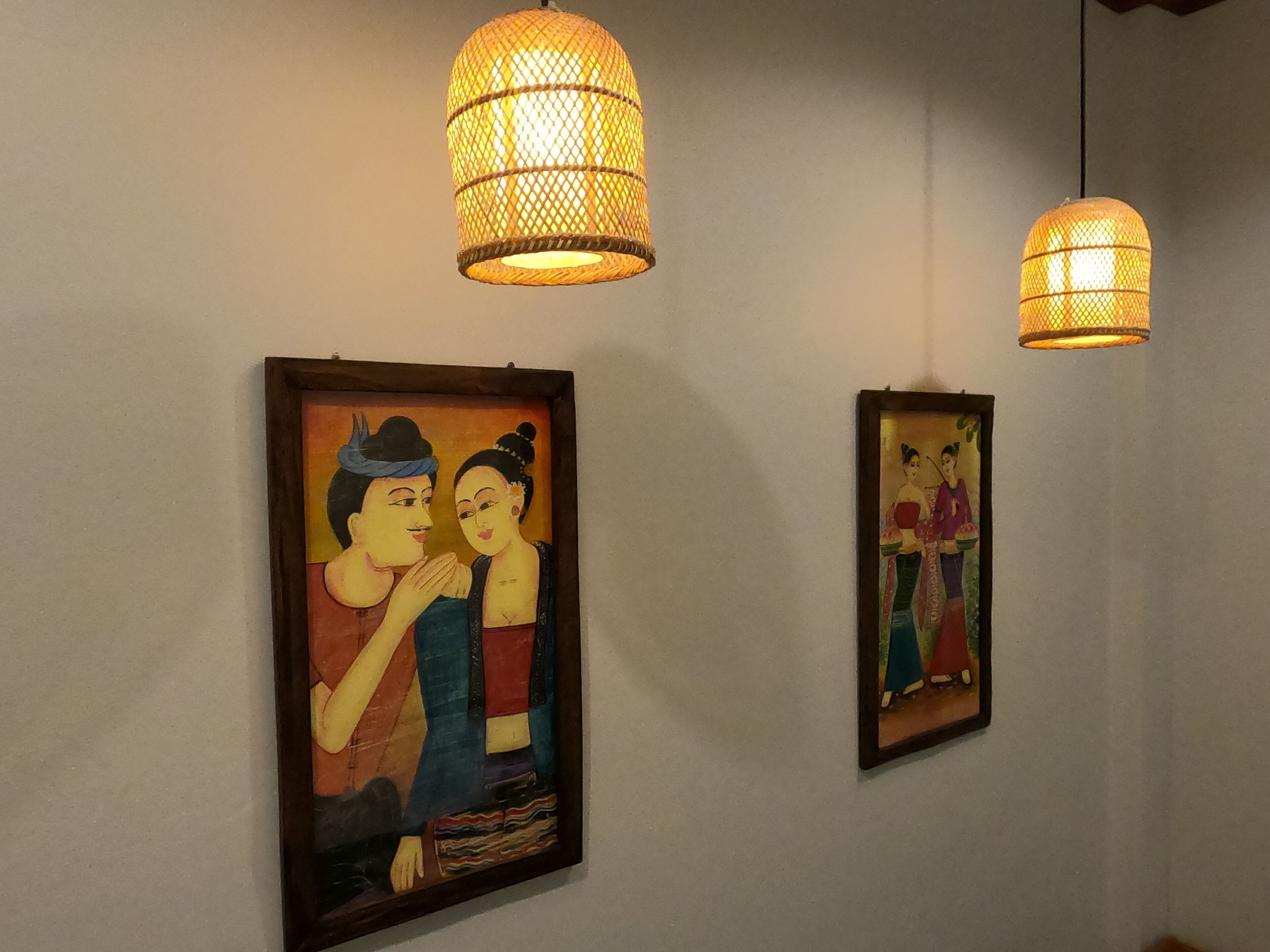 Twee ingekaderde schilderijen aan een muur, elk met een hanglamp erboven.