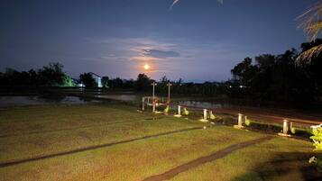 A nighttime landscape with a field, a road, and a building in the distance.
