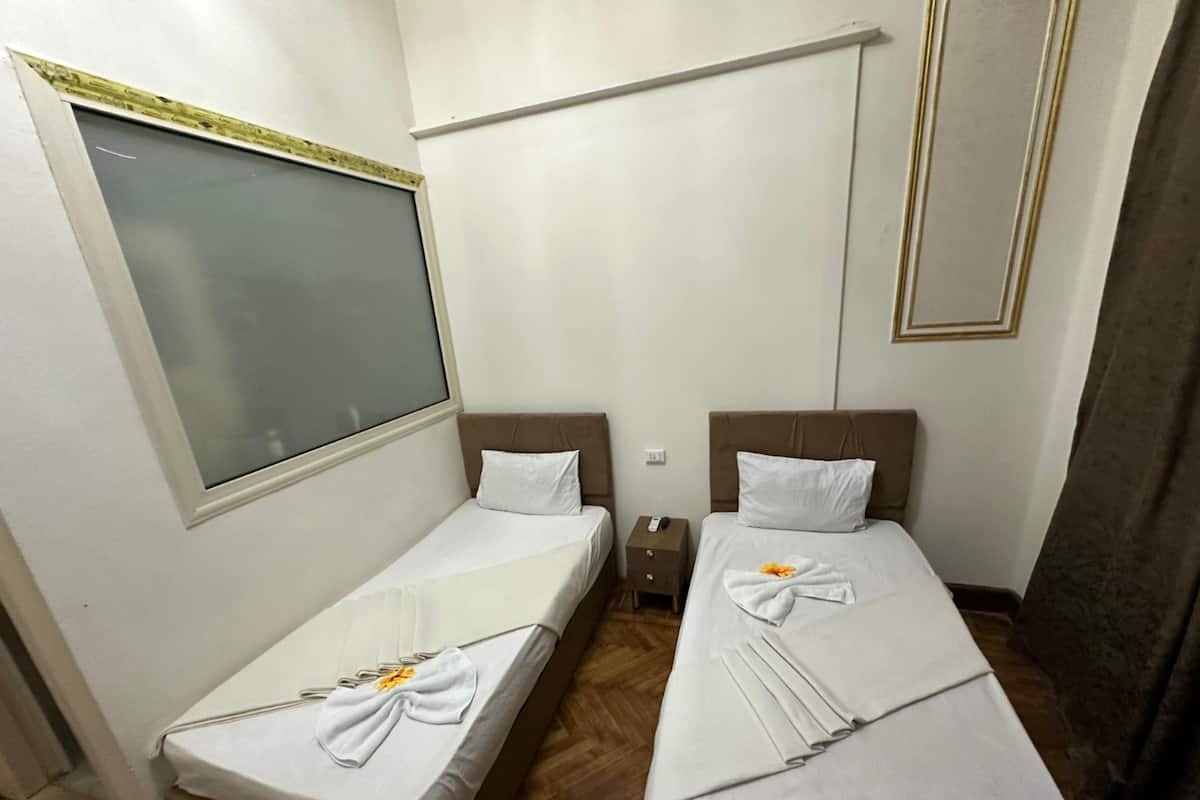 A hotel room with two single beds, a window with blinds, a nightstand, and a remote control.