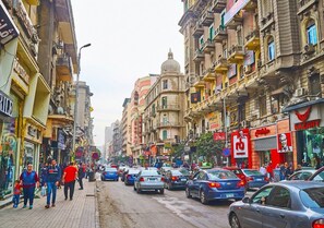 A busy urban street with pedestrians, cars, and multi-story buildings with commercial establishments. - Yacoubian Hotels (Cairo)