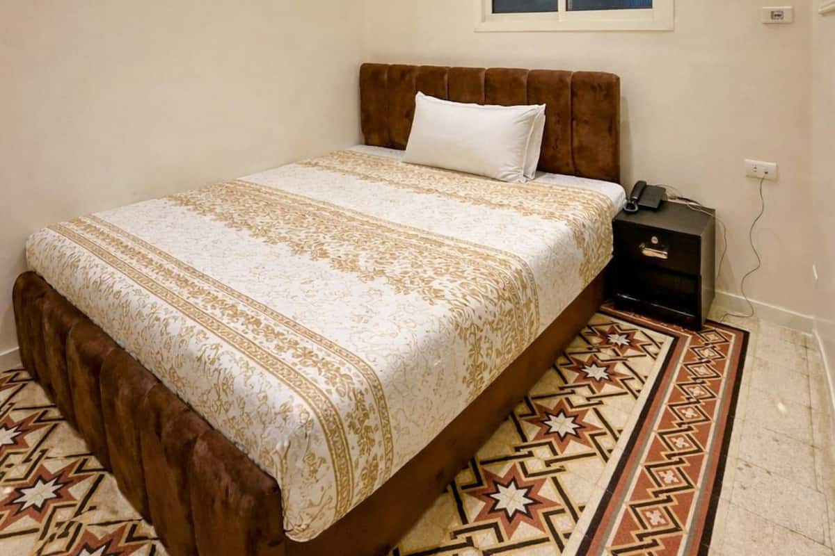 A bedroom with a bed, a nightstand, a window, and a patterned rug.