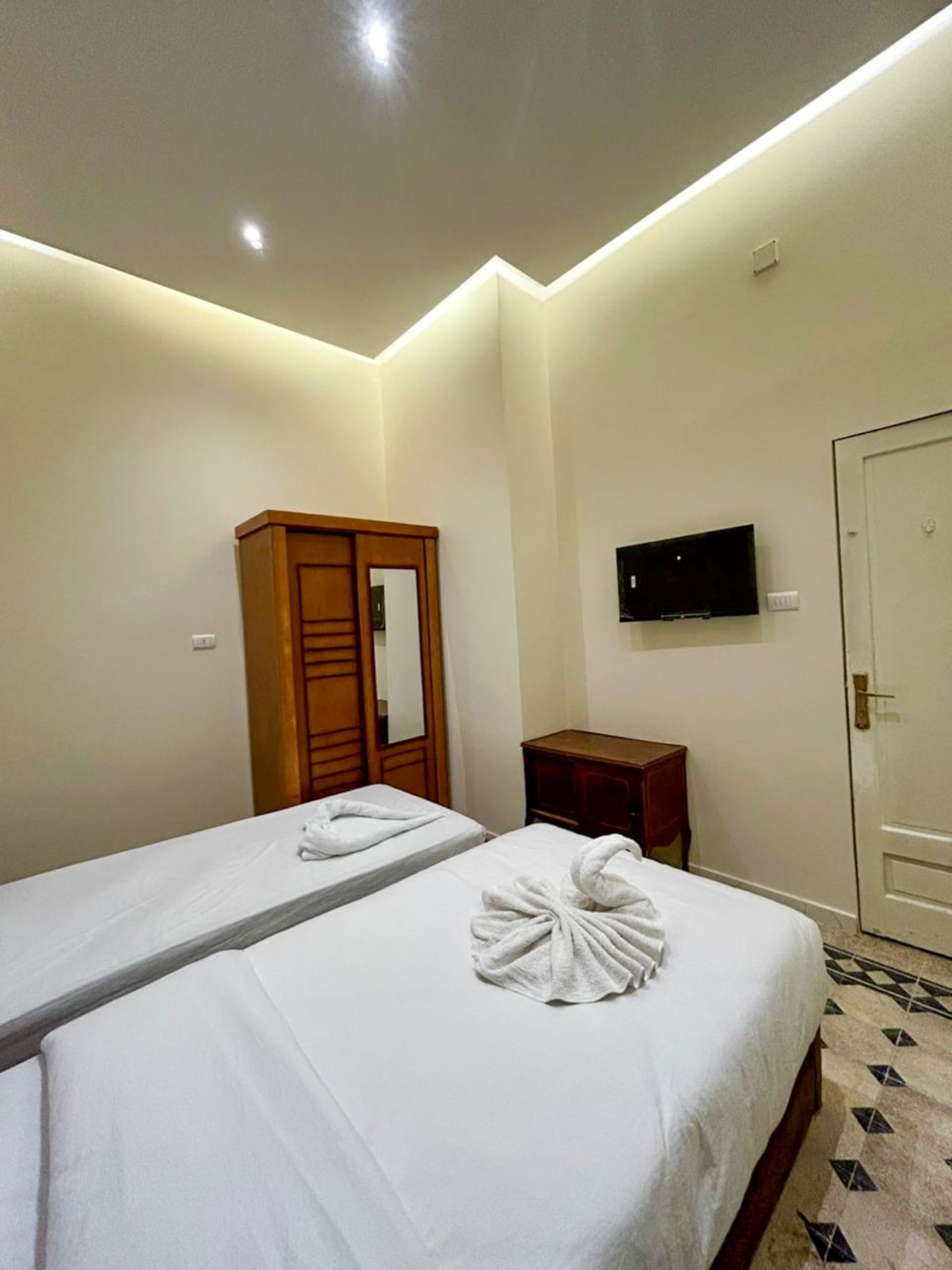 Une chambre d’hôtel avec deux lits, une armoire en bois, une télévision et une porte.