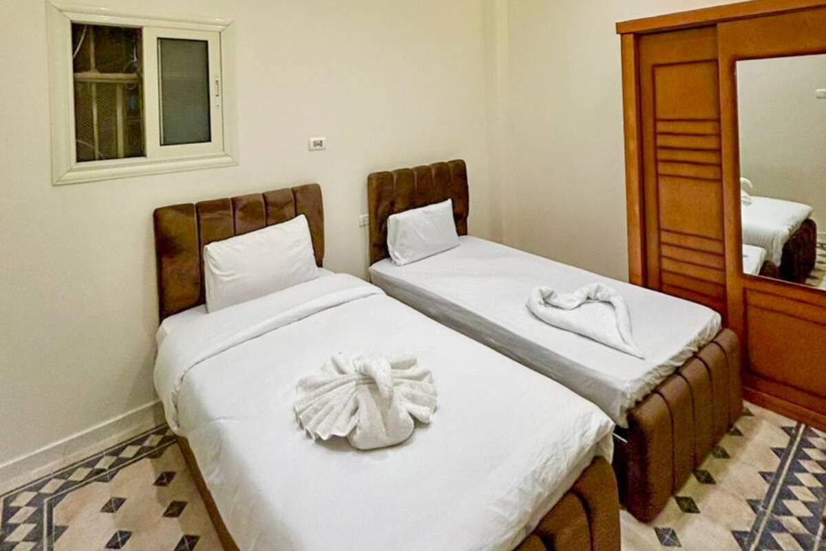 A hotel room with two beds, a window, a mirror, and a patterned floor.