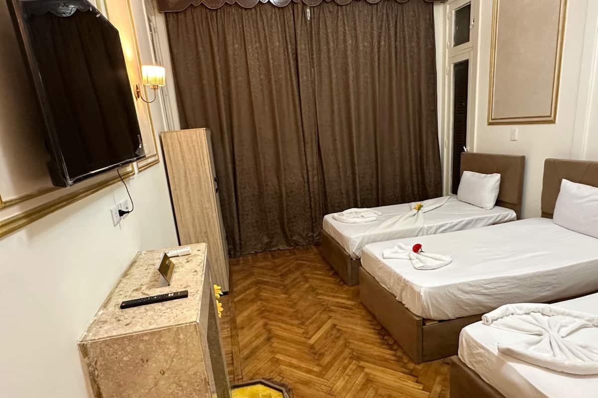 A hotel room with two beds, a TV, a desk with a computer, and a wooden herringbone floor.