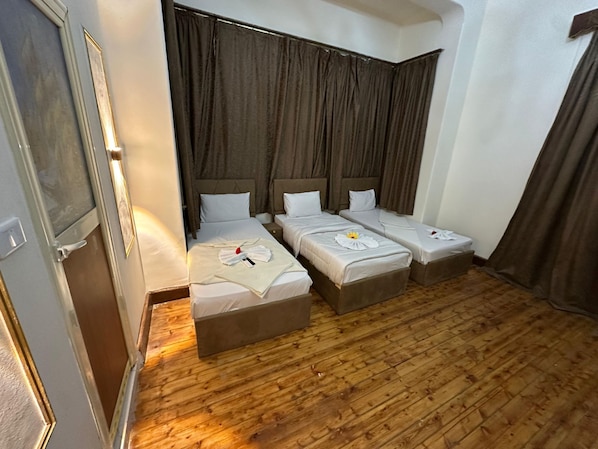 A hotel room with three beds, a wooden floor, and a large window with curtains. - Yacoubian Hotels (Cairo)