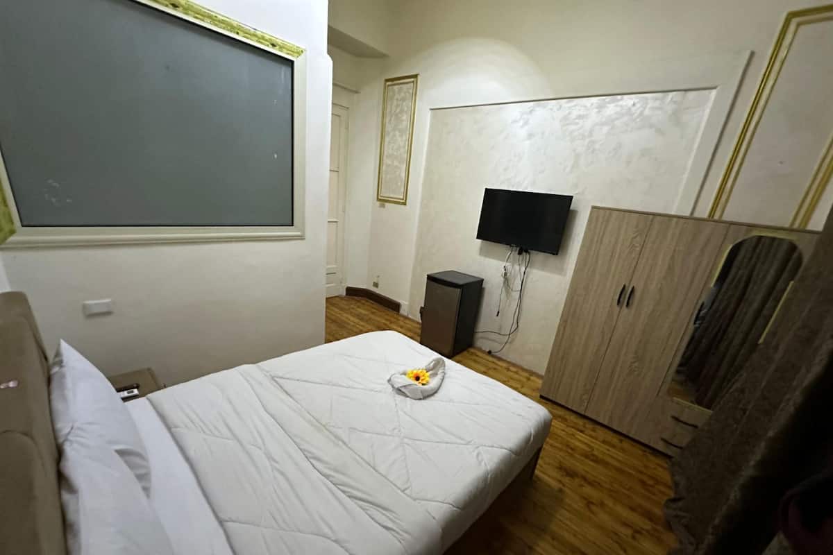 A hotel room with a bed, a wardrobe, a television, and a small cabinet.
