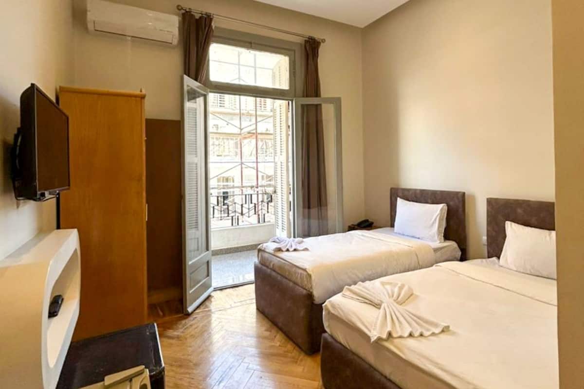 A hotel room with two beds, a TV, a wardrobe, and a window with curtains.