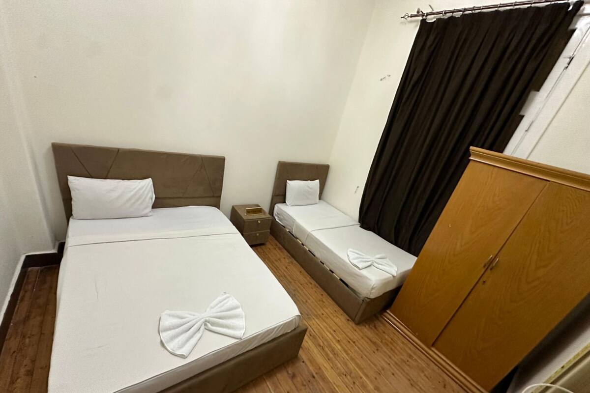 A hotel room with a large bed, a smaller bed, a wooden wardrobe, and a nightstand.