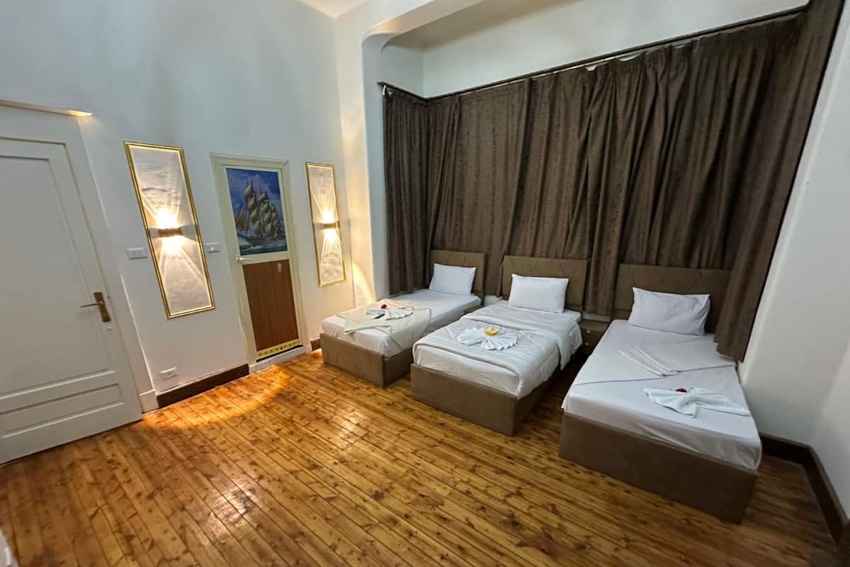 A hotel room with three beds, wooden flooring, and two wall-mounted light fixtures.