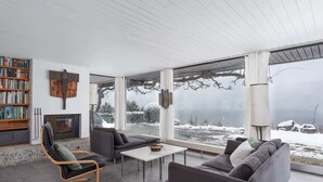Una sala de estar moderna con chimenea, una estantería y vistas a un paisaje nevado.