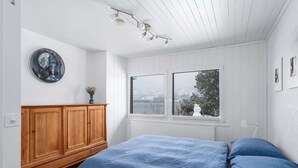 Un dormitorio con cama, armario de madera y ventana con vistas a árboles y montañas.