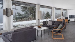 Una sala de estar moderna con un sofá, una mesa de centro y un sillón. Se ve un televisor y un aparador al fondo.