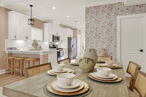 A modern kitchen with white cabinetry, a central island, and a dining area with a wooden table set for six. - Cozy Home by Medical Center and Downtown! Lydia A (Houston)