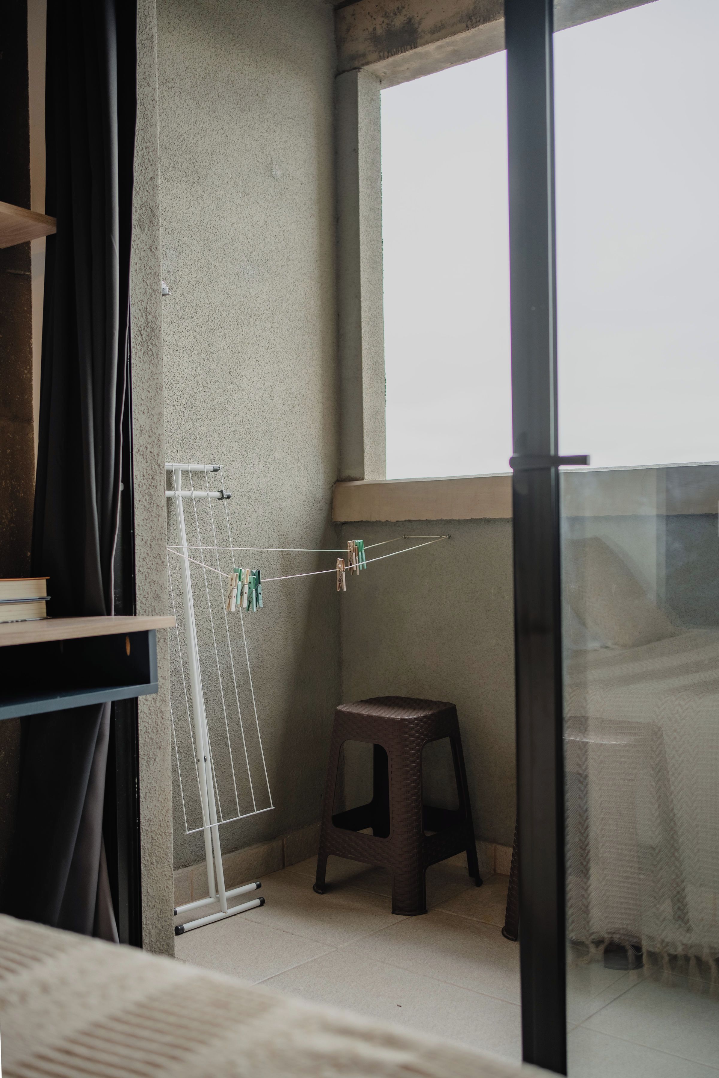 A balcony with a clothes drying rack, a small stool, and a window.