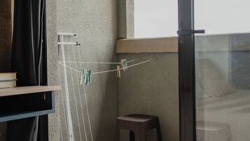 A balcony with a clothes drying rack, a small stool, and a window.
