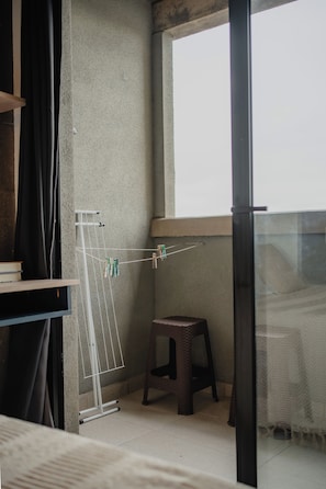 Un balcon avec un étendoir, un petit tabouret et une fenêtre.