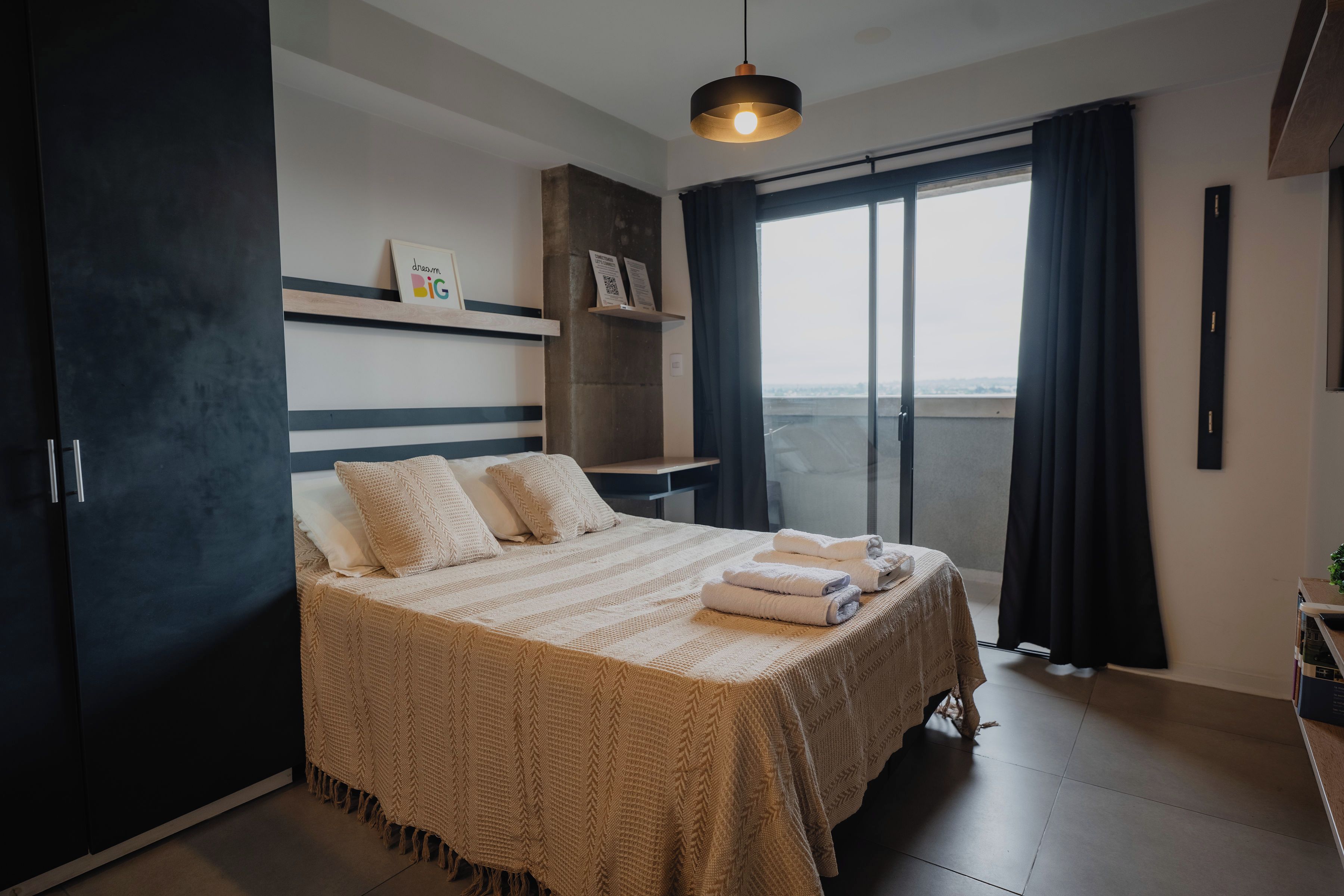 Un dormitorio moderno con una cama grande, una mesita de noche, una lámpara colgante y vistas amplias por un ventanal.