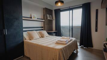 Un dormitorio moderno con una cama grande, una mesita de noche, una lámpara colgante y vistas amplias por un ventanal.