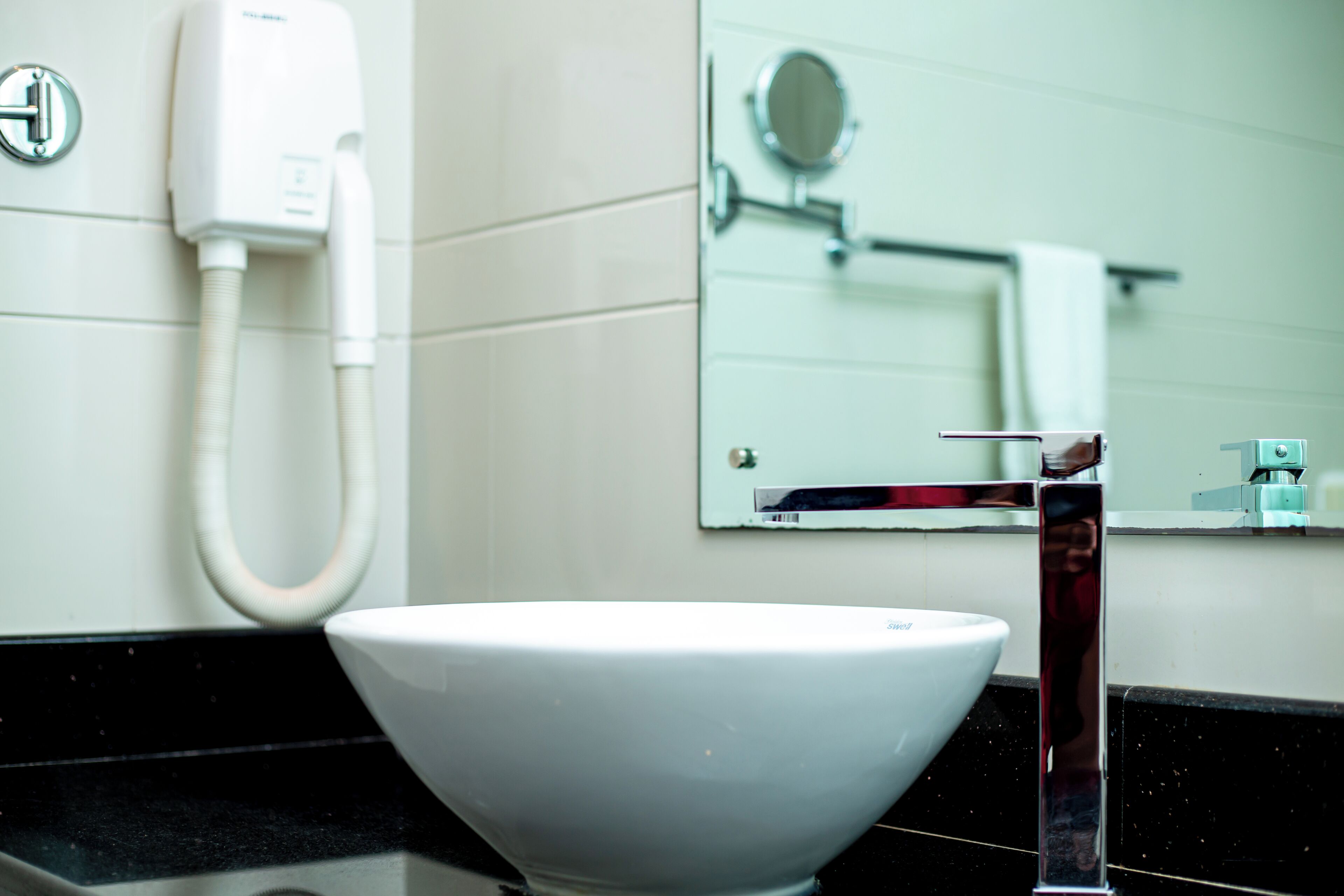 A bathroom with a white sink, a mirror, a towel rack, and a hand dryer.