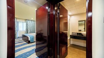 Una habitación de hotel con cama, baño con lavamanos y espejo, y piso alfombrado.