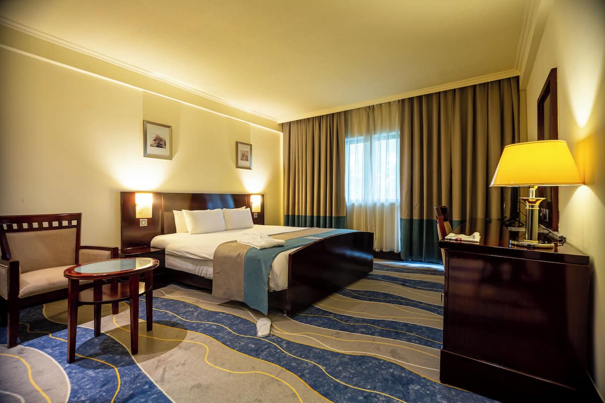A hotel room with a bed, a desk, a chair, a lamp, and a picture on the wall.