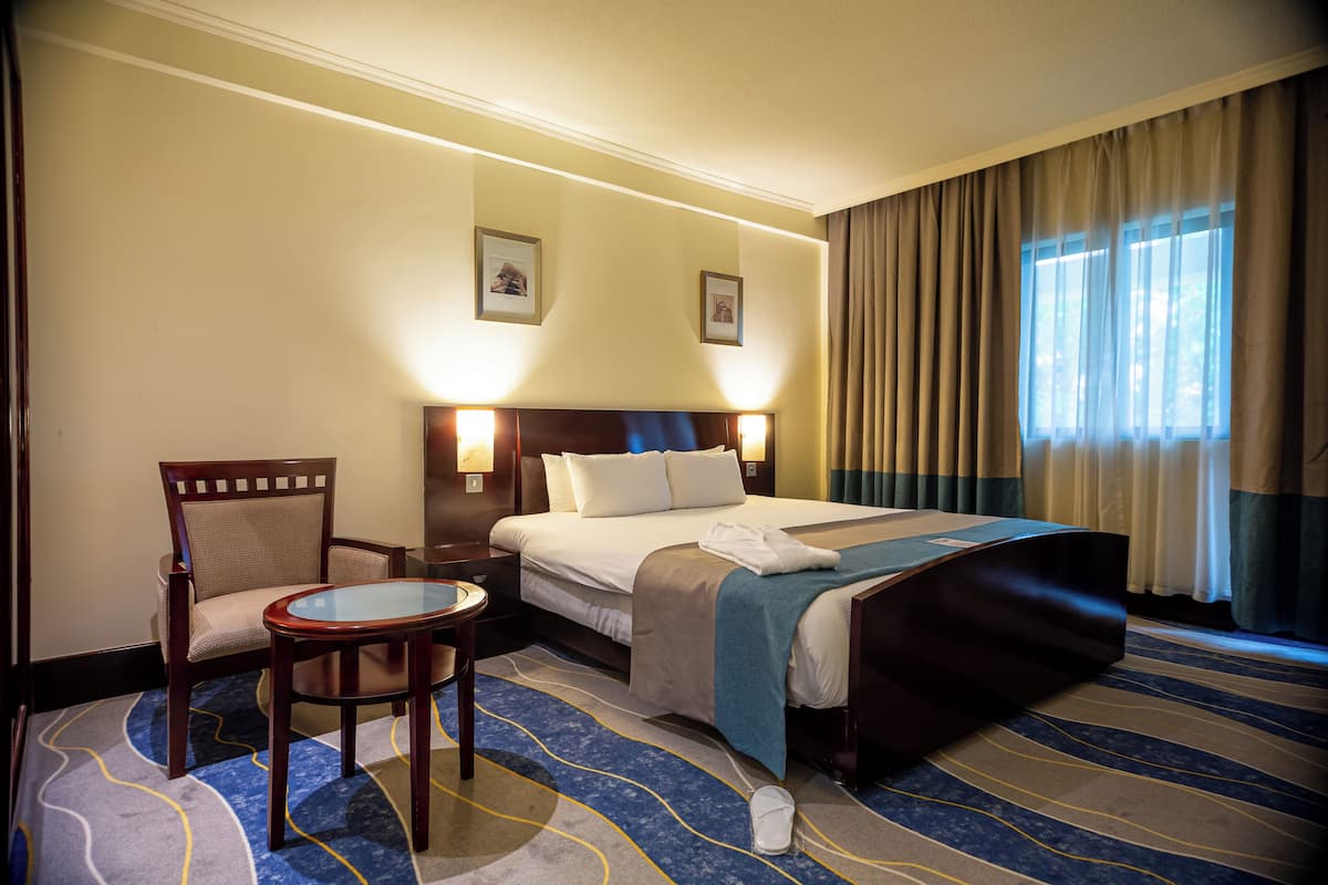 A hotel room with a bed, a chair, a small table, and a window with curtains.