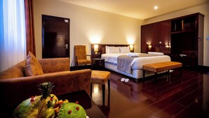 Una habitación de hotel con cama, sofá, sillón, mesita de noche y un armario de madera.