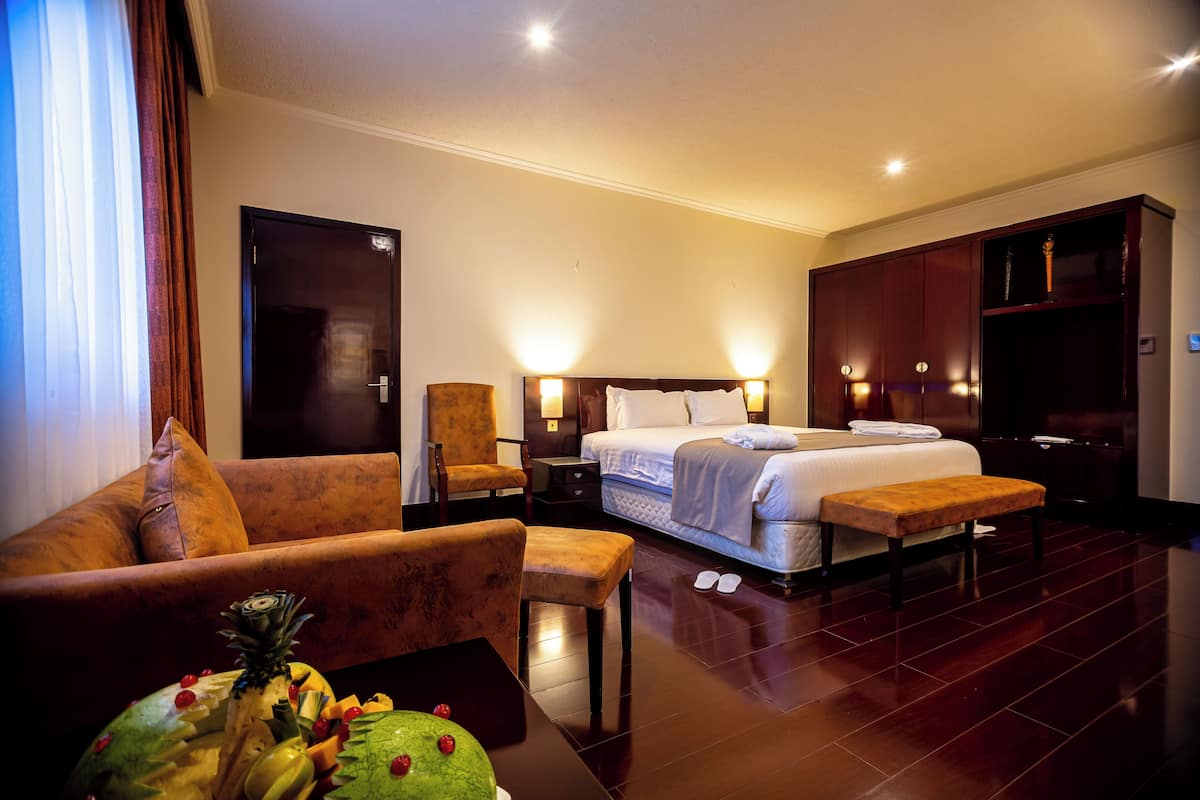 A hotel room with a bed, a sofa, a chair, a nightstand, and a wooden cabinet.