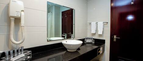 A modern bathroom with a black countertop, a white sink, a handheld showerhead, a mirror, and a dark wooden door.