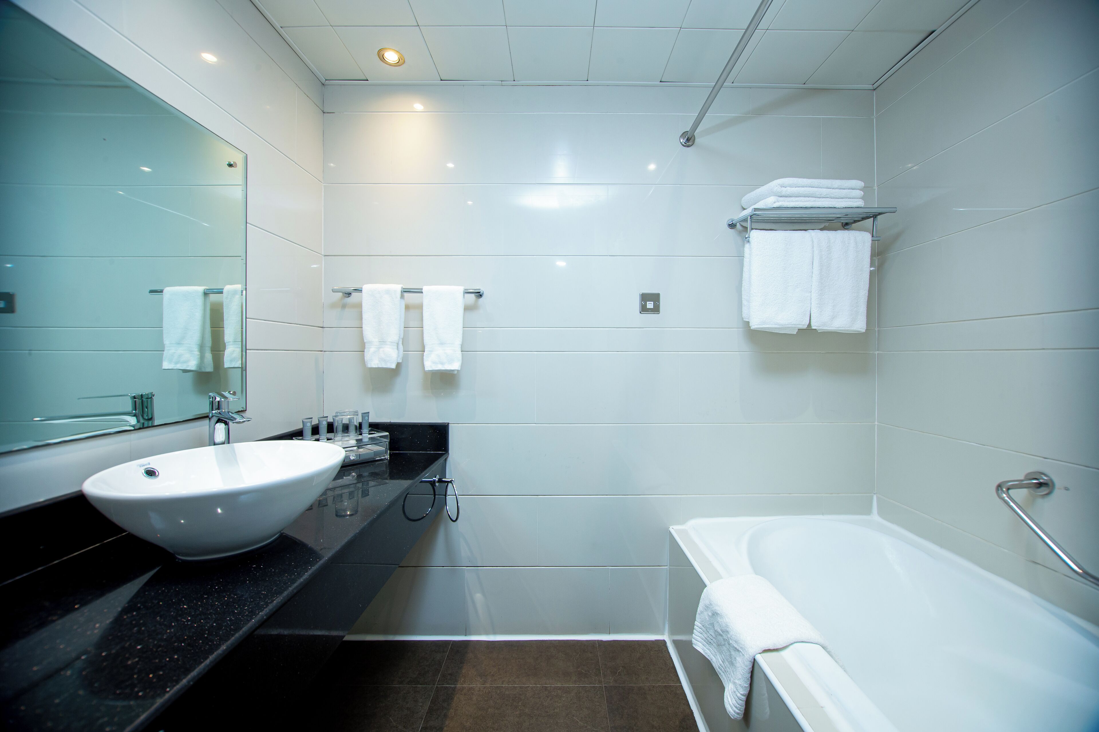 A modern bathroom with a large white sink, a bathtub, and a mirror.