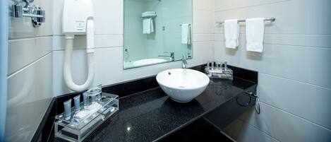 Un baño moderno con lavamanos blanco, ducha con cerramiento de vidrio y espejo sobre el lavamanos.