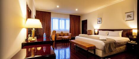 A hotel room with a bed, a desk, a chair, a bench, a nightstand, and a lamp.