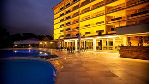 Un hotel de varios pisos con área de piscina, mobiliario exterior y un bar.