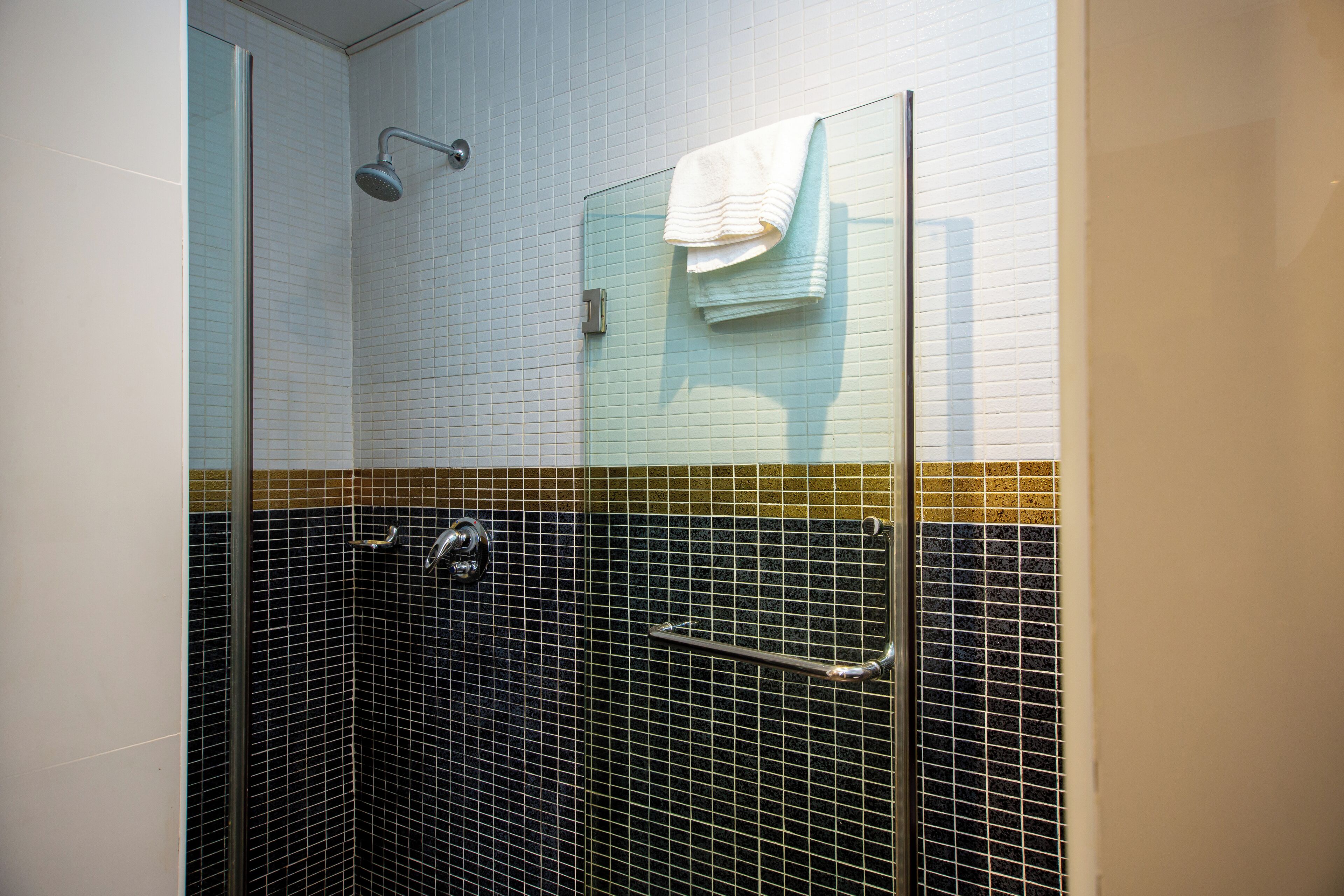 A glass-enclosed shower with a handrail, a towel rack with a folded towel, and a tiled wall with a yellow and black pattern.