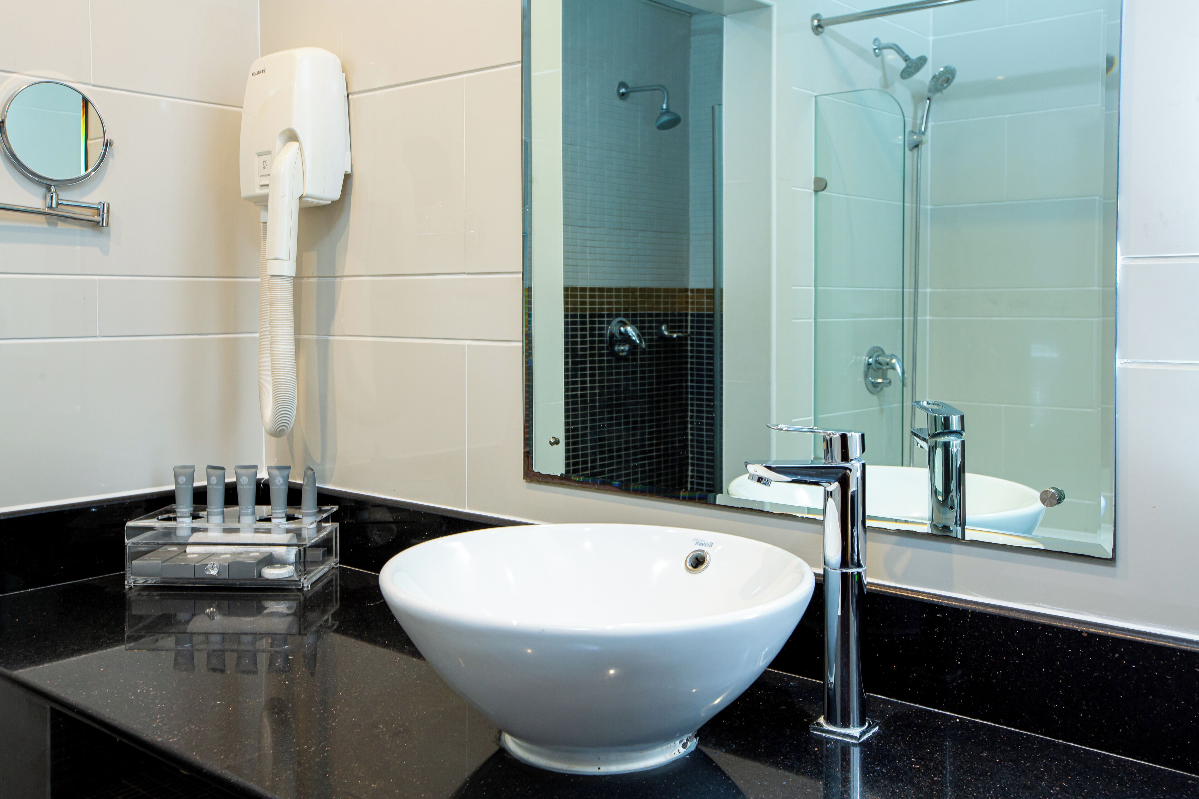 A bathroom with a white sink, a handheld showerhead, a towel rack, and a mirror.