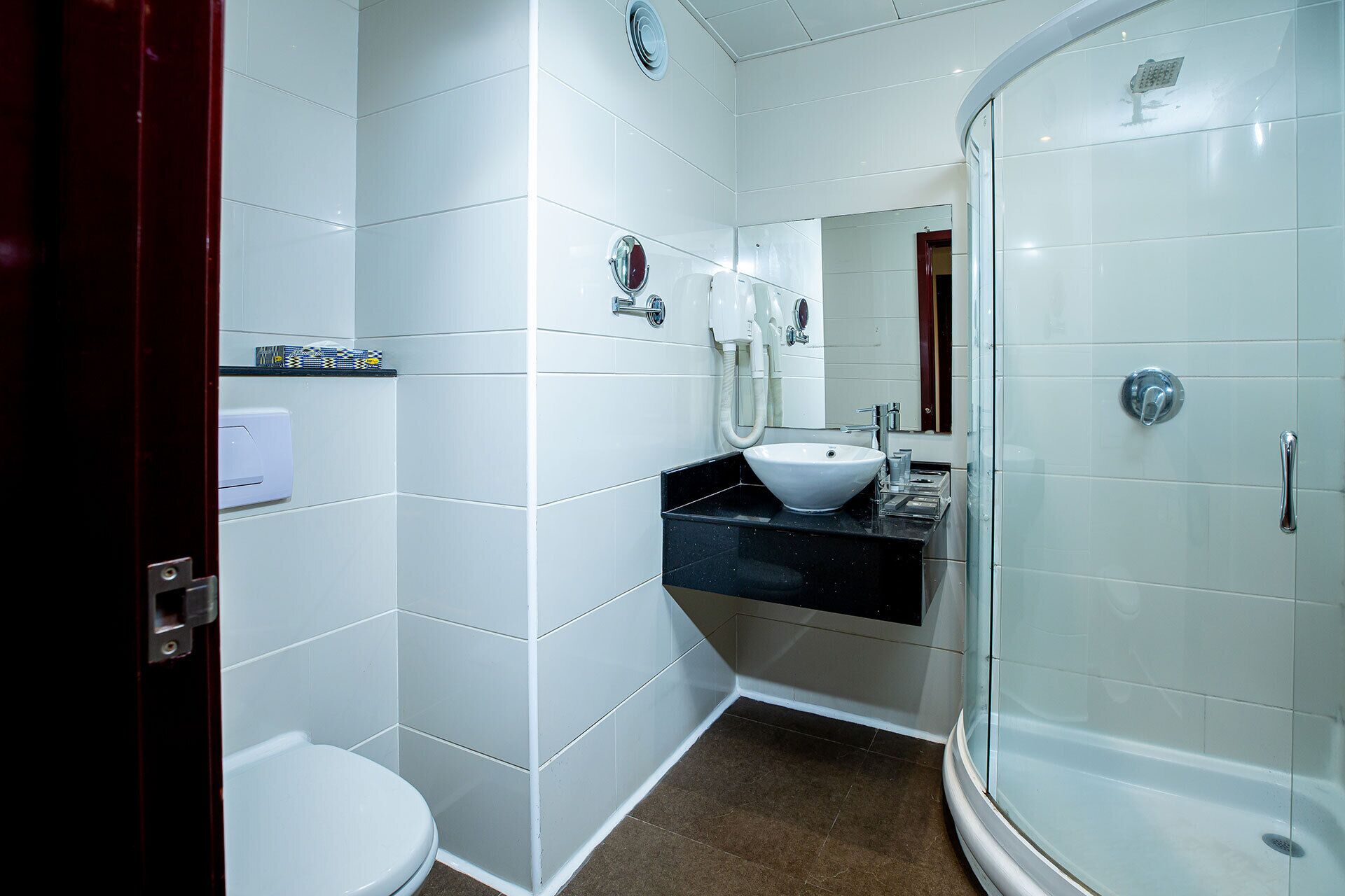 A modern bathroom with white tiles, a white sink, a toilet, and a glass-enclosed shower.