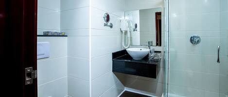 A modern bathroom with white tiles, a white sink, a toilet, and a glass-enclosed shower.