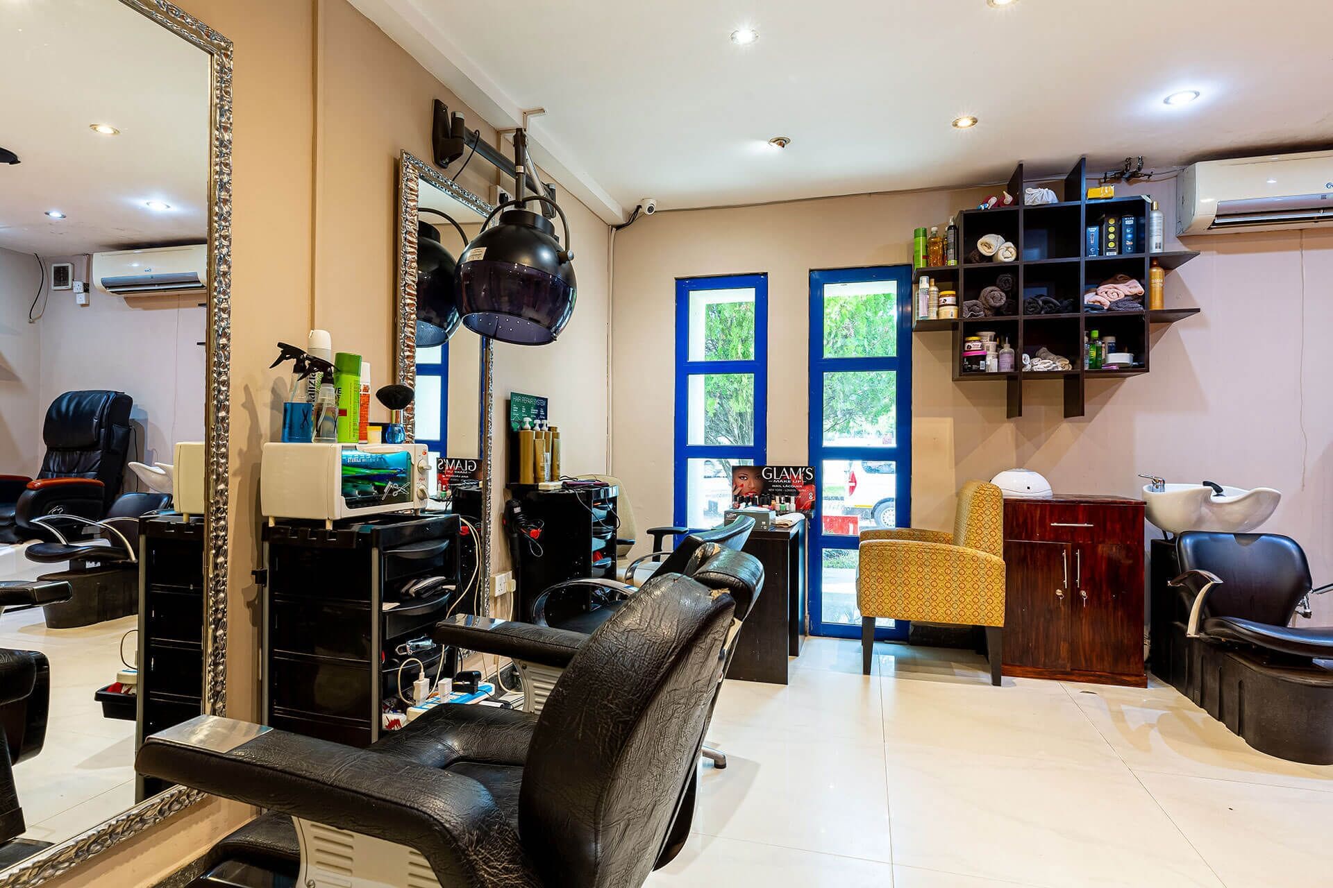 A salon with a large mirror, black leather chairs, shelves with hair products, and a view of the outside through a window.