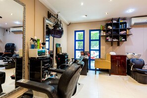 A salon with a large mirror, black leather chairs, shelves with hair products, and a view of the outside through a window.