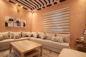 A modern living room with a sectional sofa, a wooden coffee table, and a large window with blinds. - Cosy & quiet apartment in the center of town • GROUND FLOOR - Easy access (Fès)